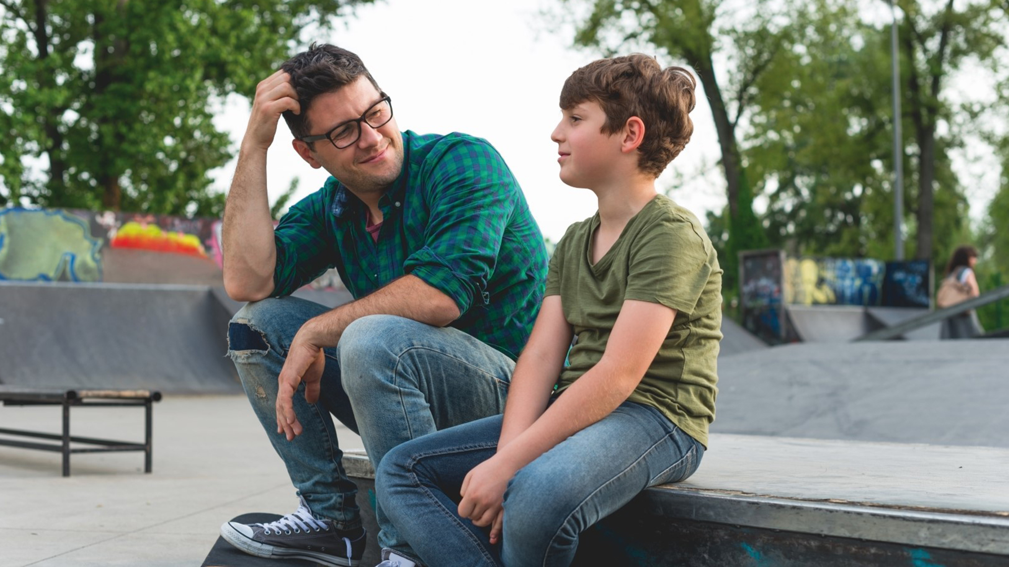 Boy and man sitting together at skate park