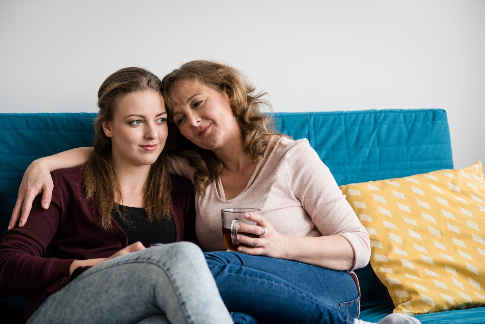 mother with arm around daughter relaxed on sofa