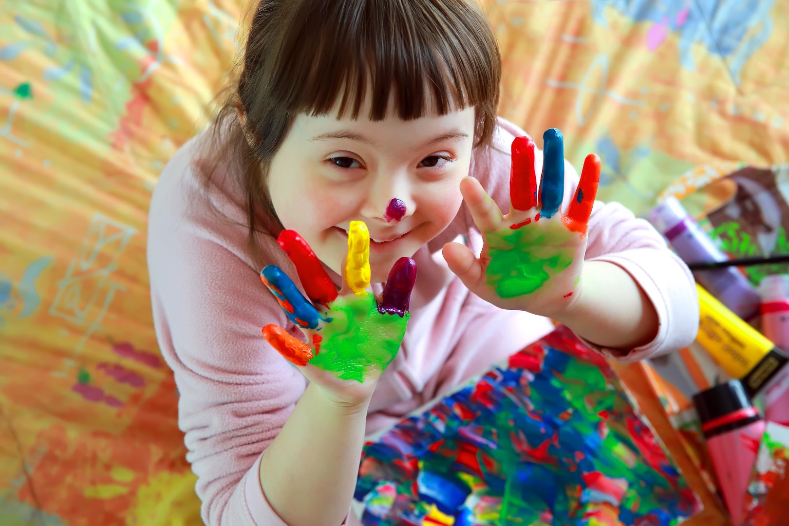 Child with different coloured paints on their hands, smiling