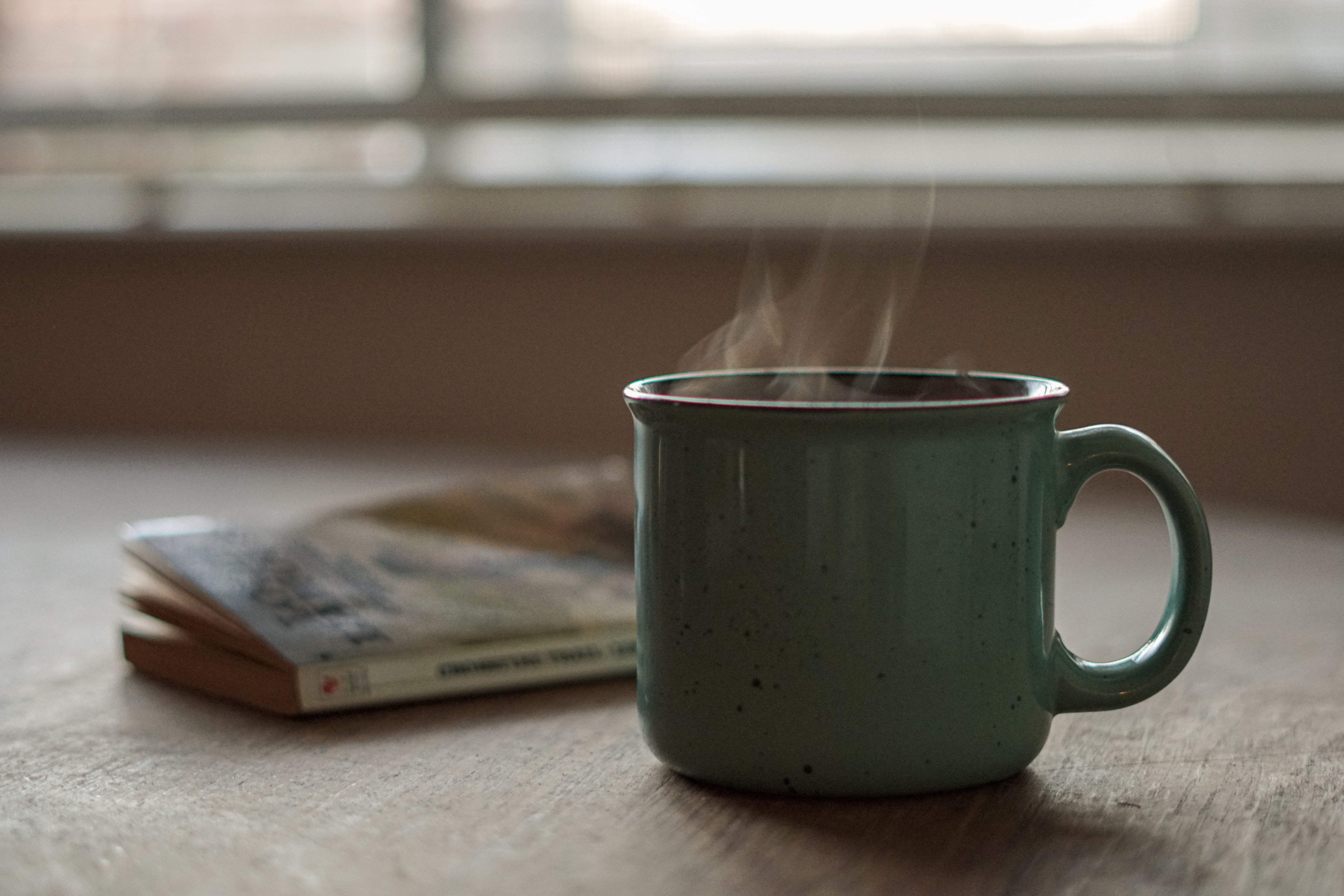 Mug of steaming coffee and book on a table
