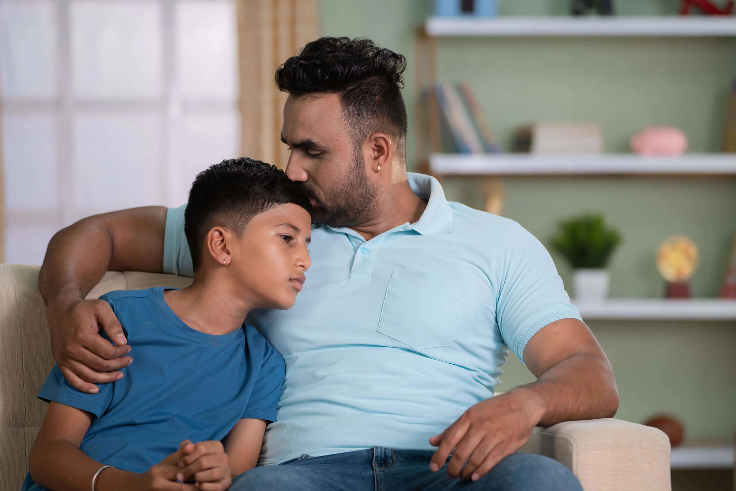 Male father figure kissing younger male on the head in embrace