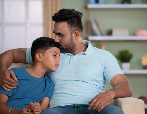 Male father figure kissing younger male on the head in embrace