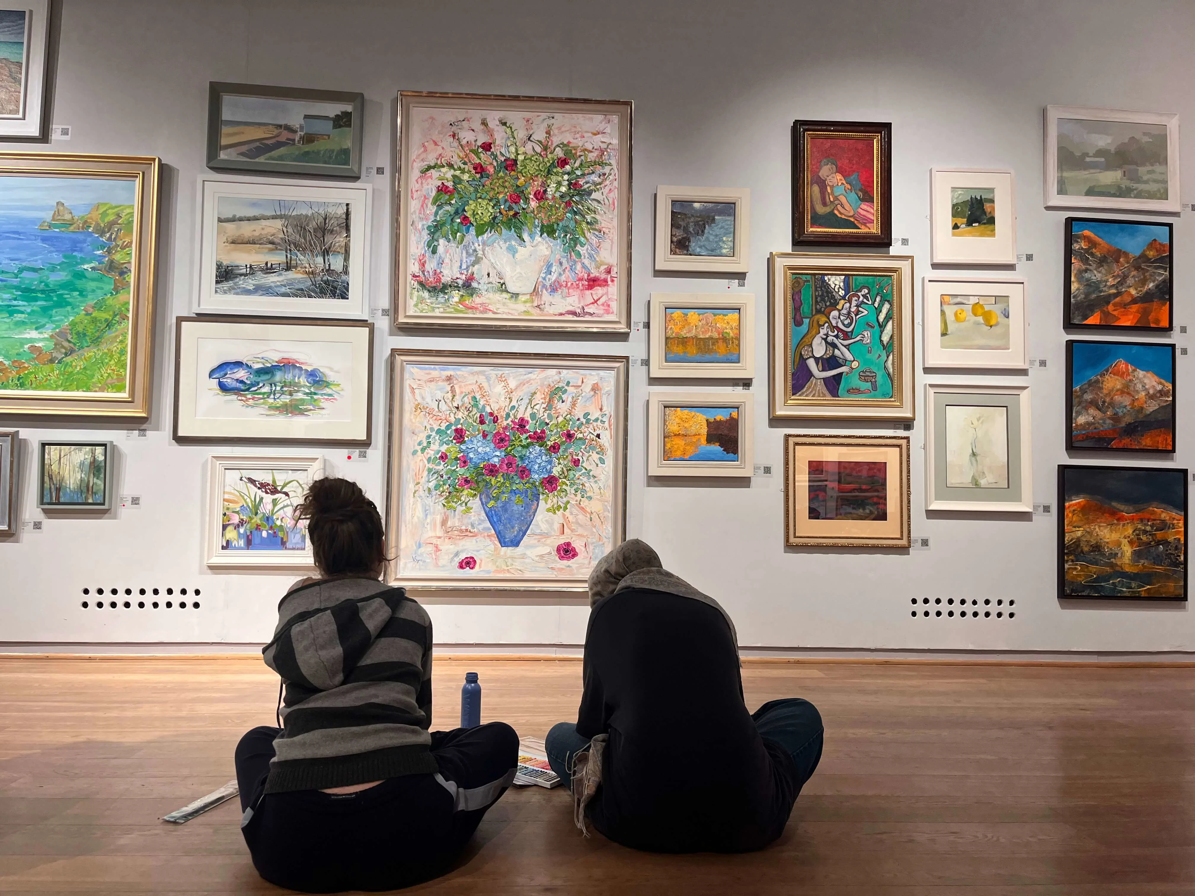 Two students sitting on the gallery floor looking at paintings