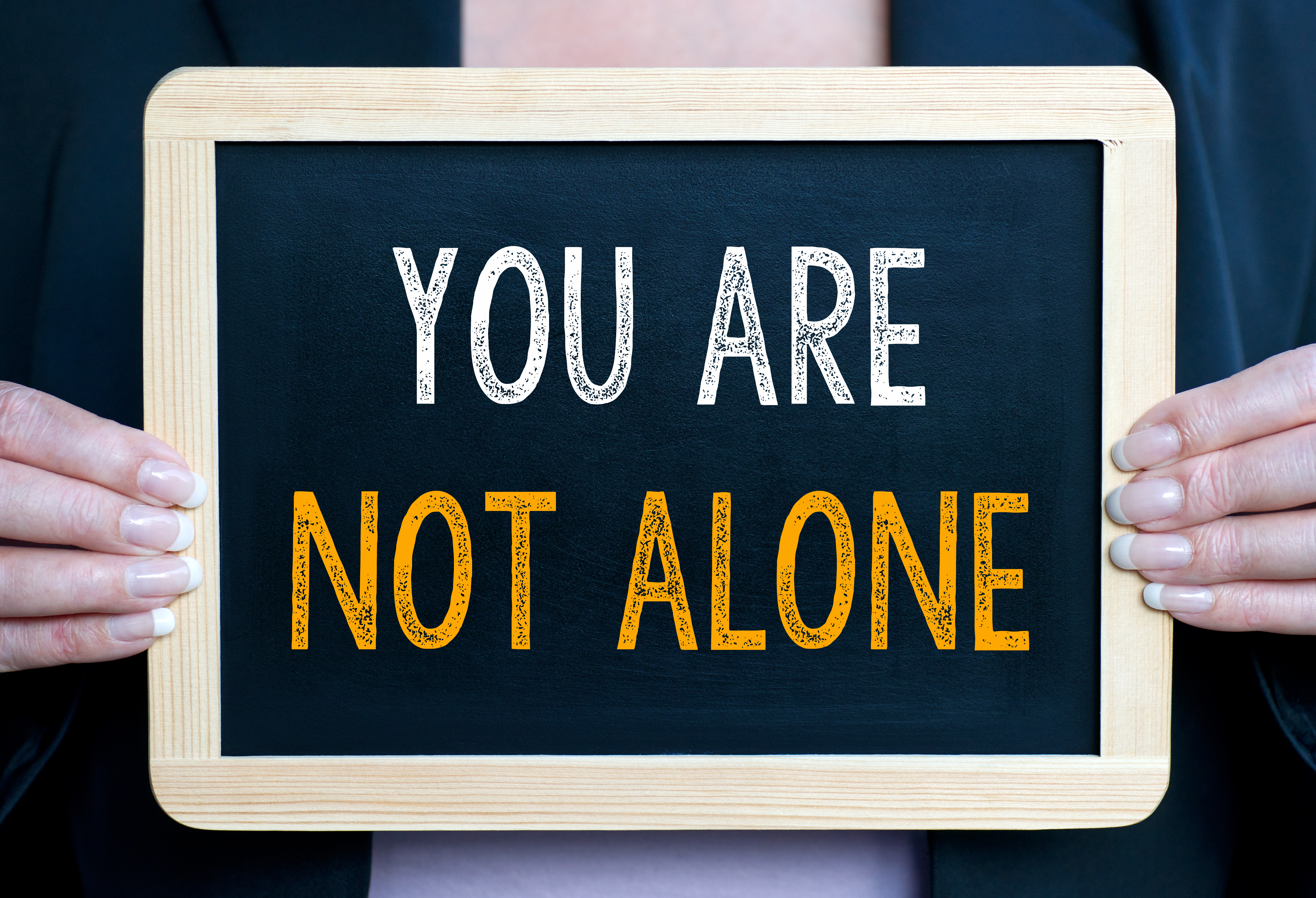 Hands hold a chalk board sign reading 'You are not alone'