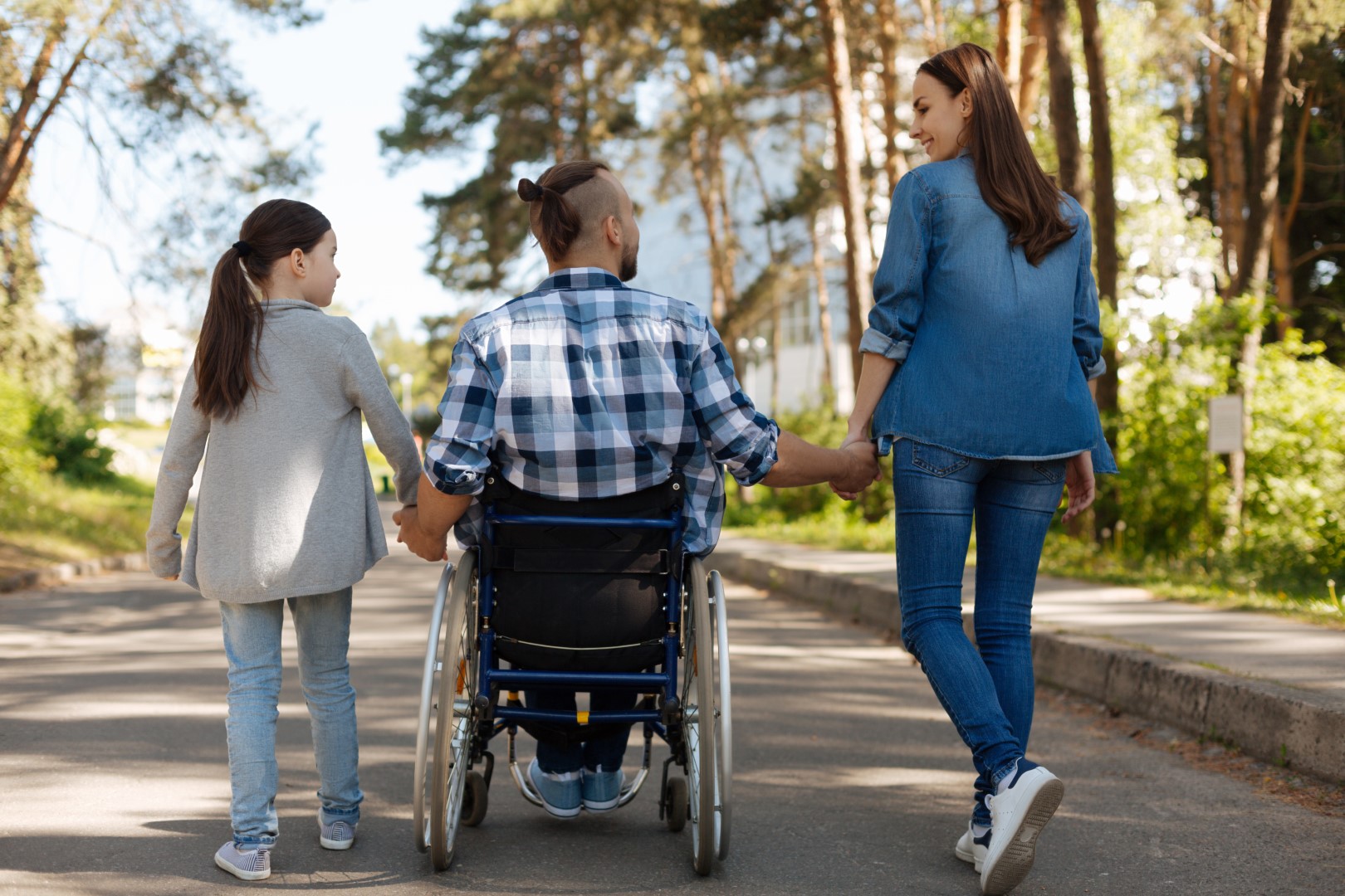 Two adults, one walking and one in a wheelchair holding hands with a young child