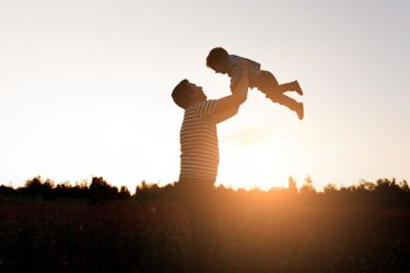 Father Holding Son In The Air With Sunset