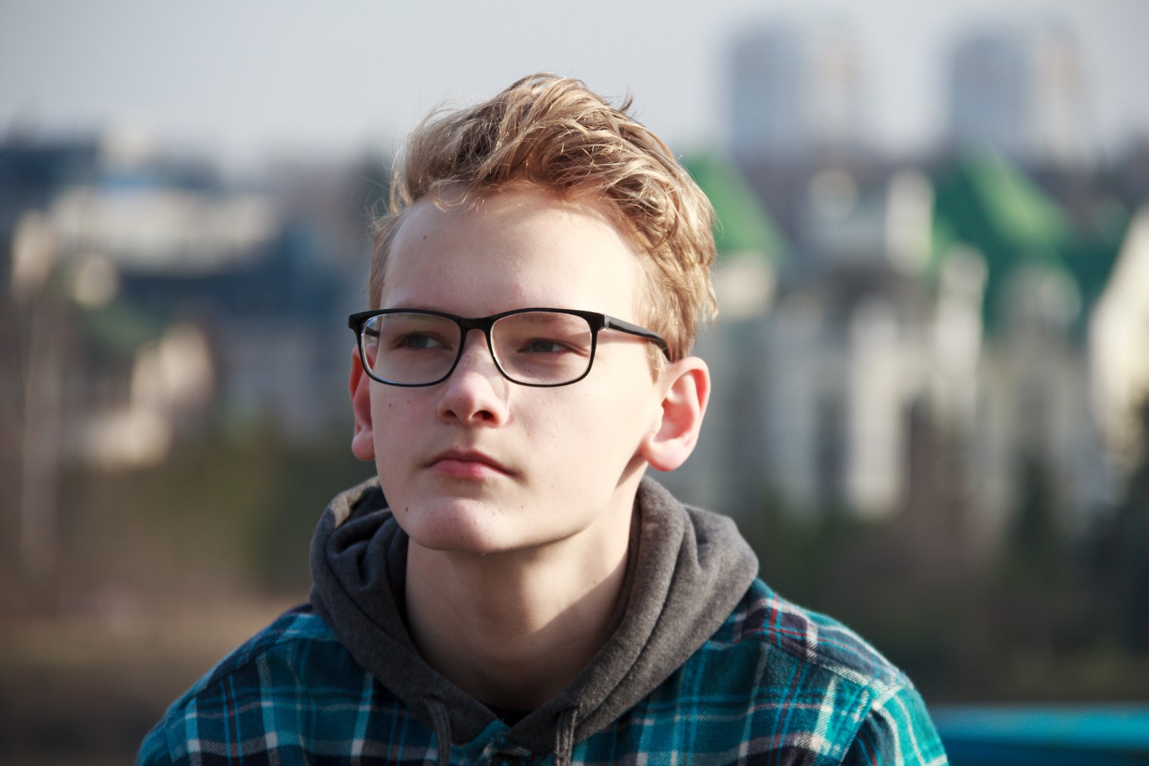 boy wearing glasses looking away, sitting outside