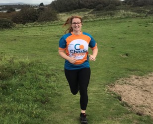 young woman running in meadow wearing Charlie Waller t-shirt