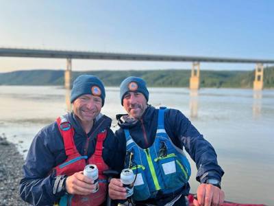 Charlie and Justin in front of a river with cans in their hands