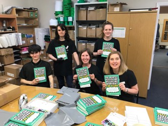 Volunteers in office wearing black t-shirts, holding books and smiling