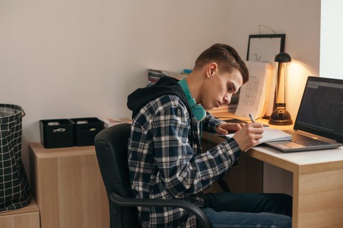 teenage boy studying at desk with headphones around his neck