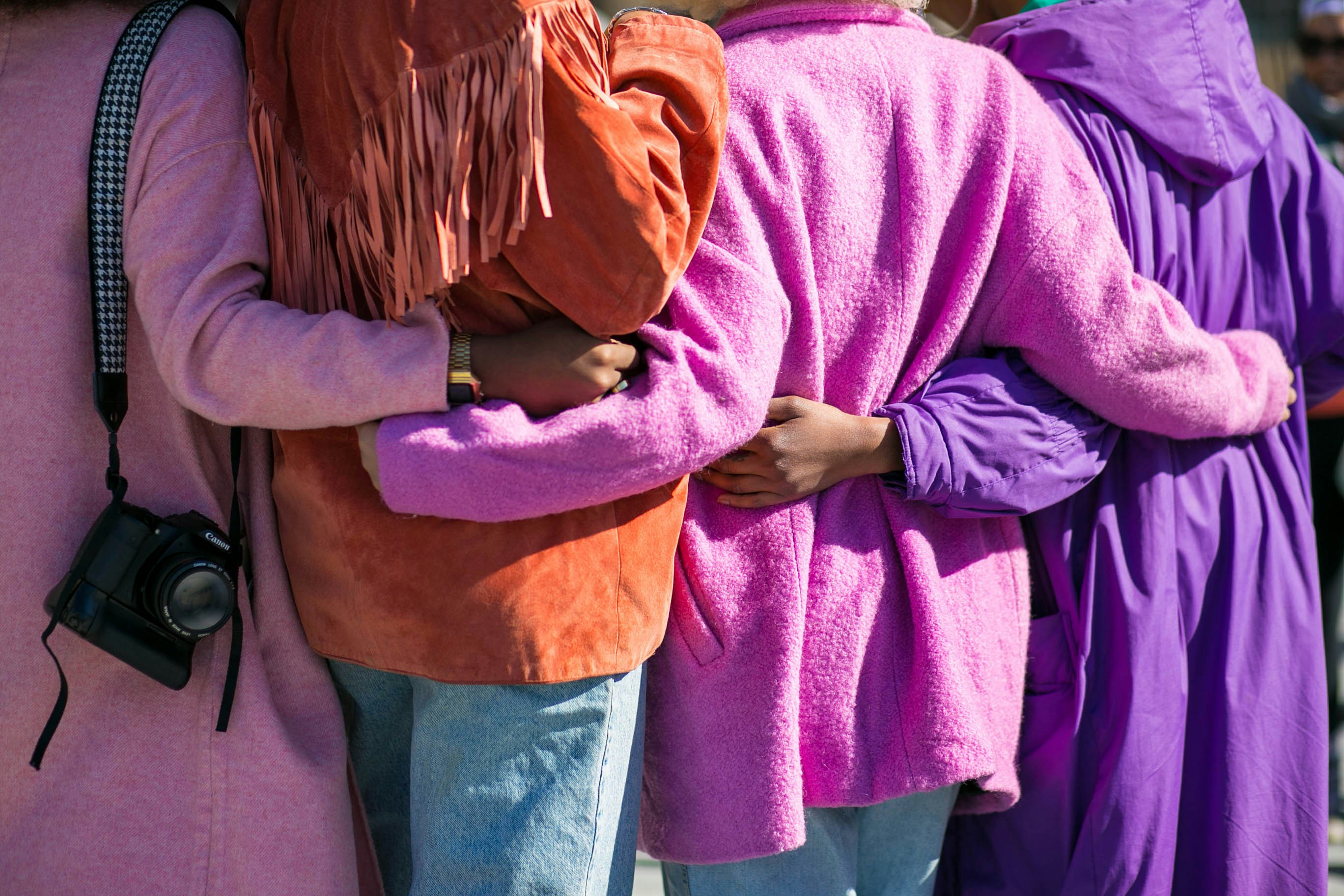 Back view of four people in brightly coloured clothes hugging each other