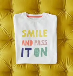 t-shirt folder on yellow cushioned background, wording reads smile and pass it on