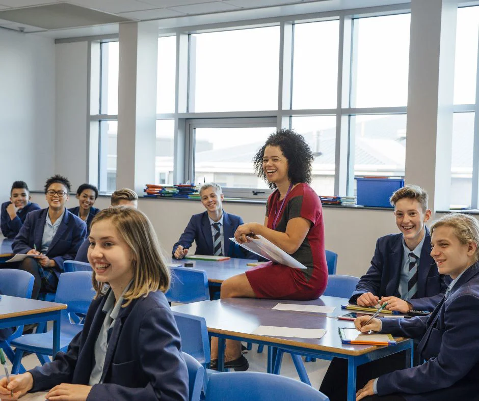 Female teacher sitting on a table in the middle of a classroom 